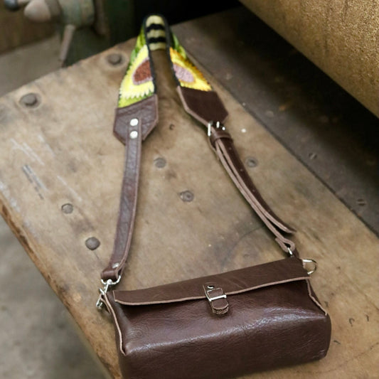 Brown leather handbag with decorative strap on a rustic wooden surface