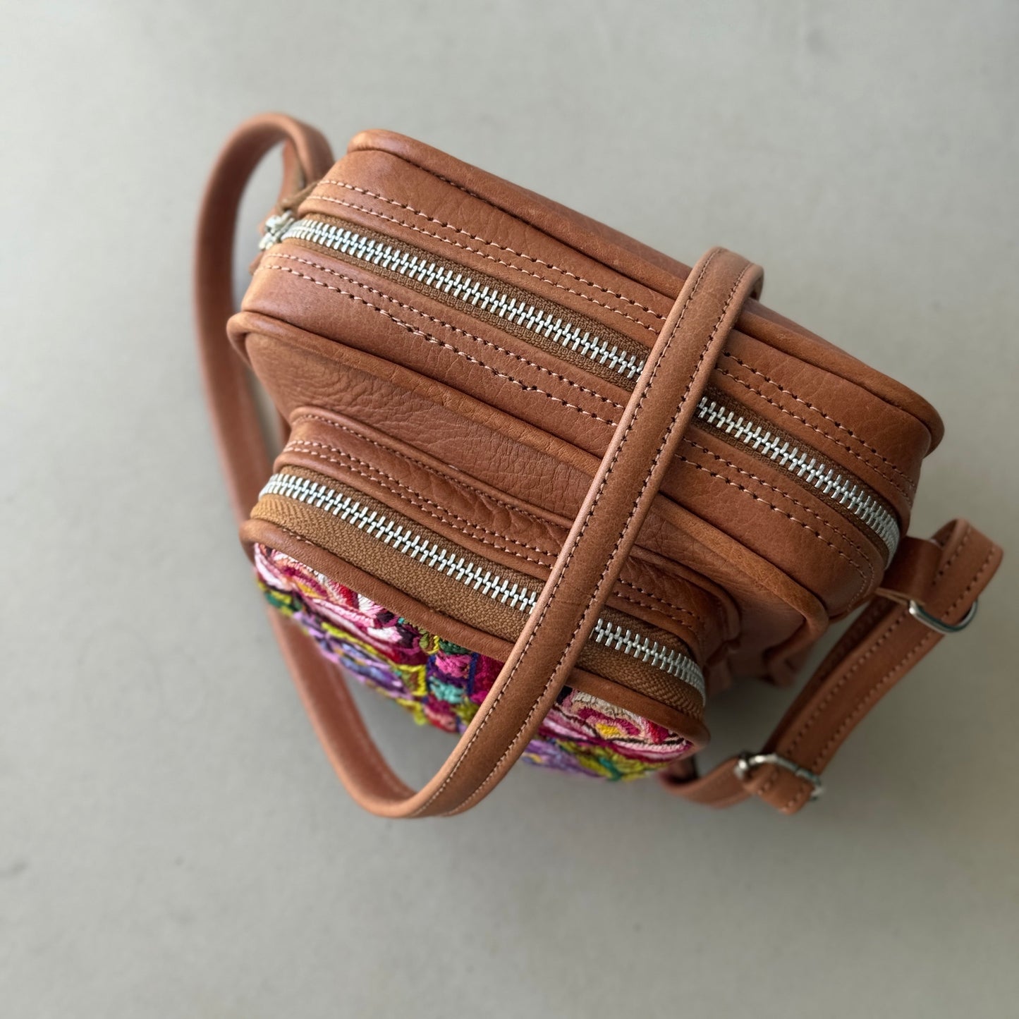 Brown leather crossbody bag with floral pattern on a light gray background