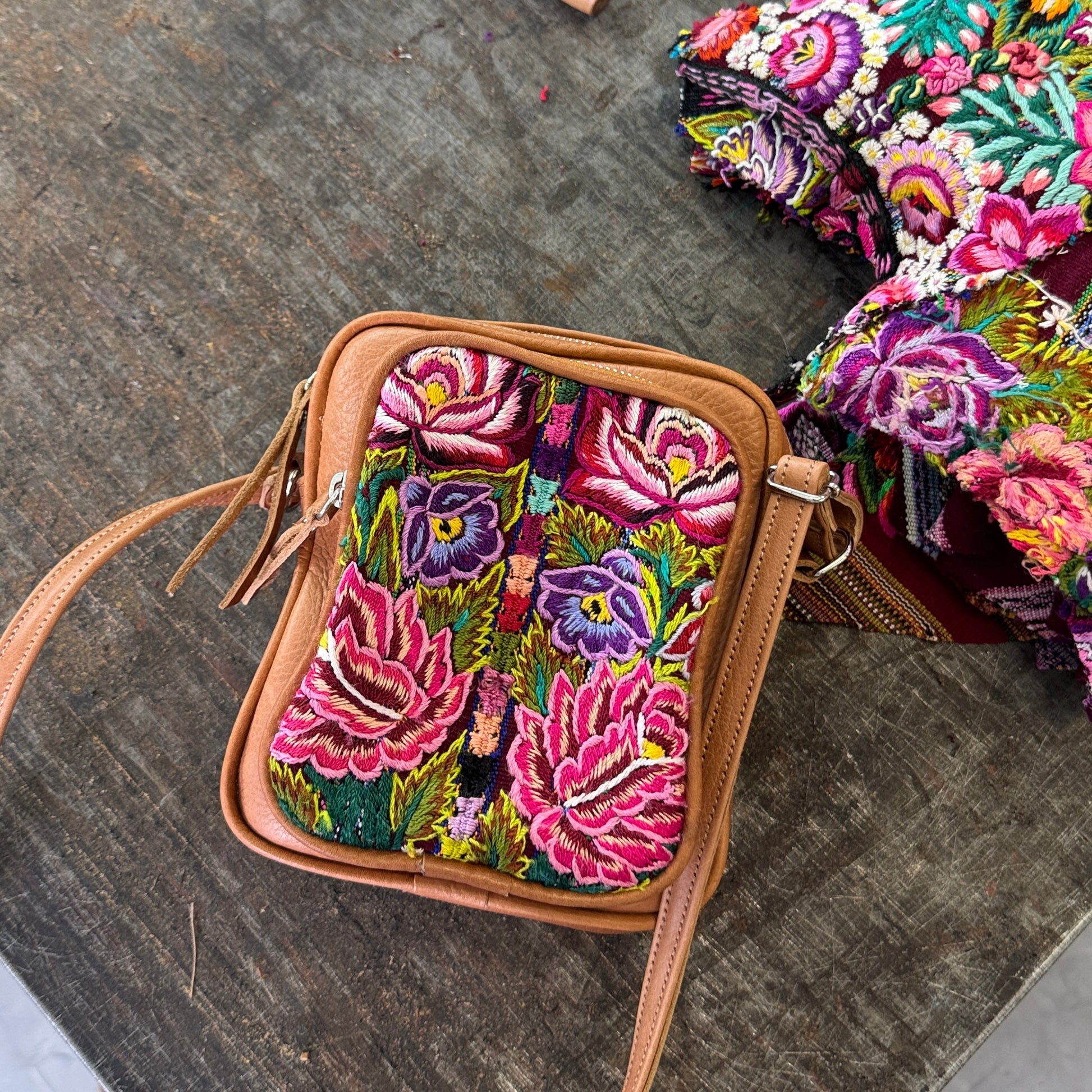 Colorful embroidered bag on a textured surface with various items around
