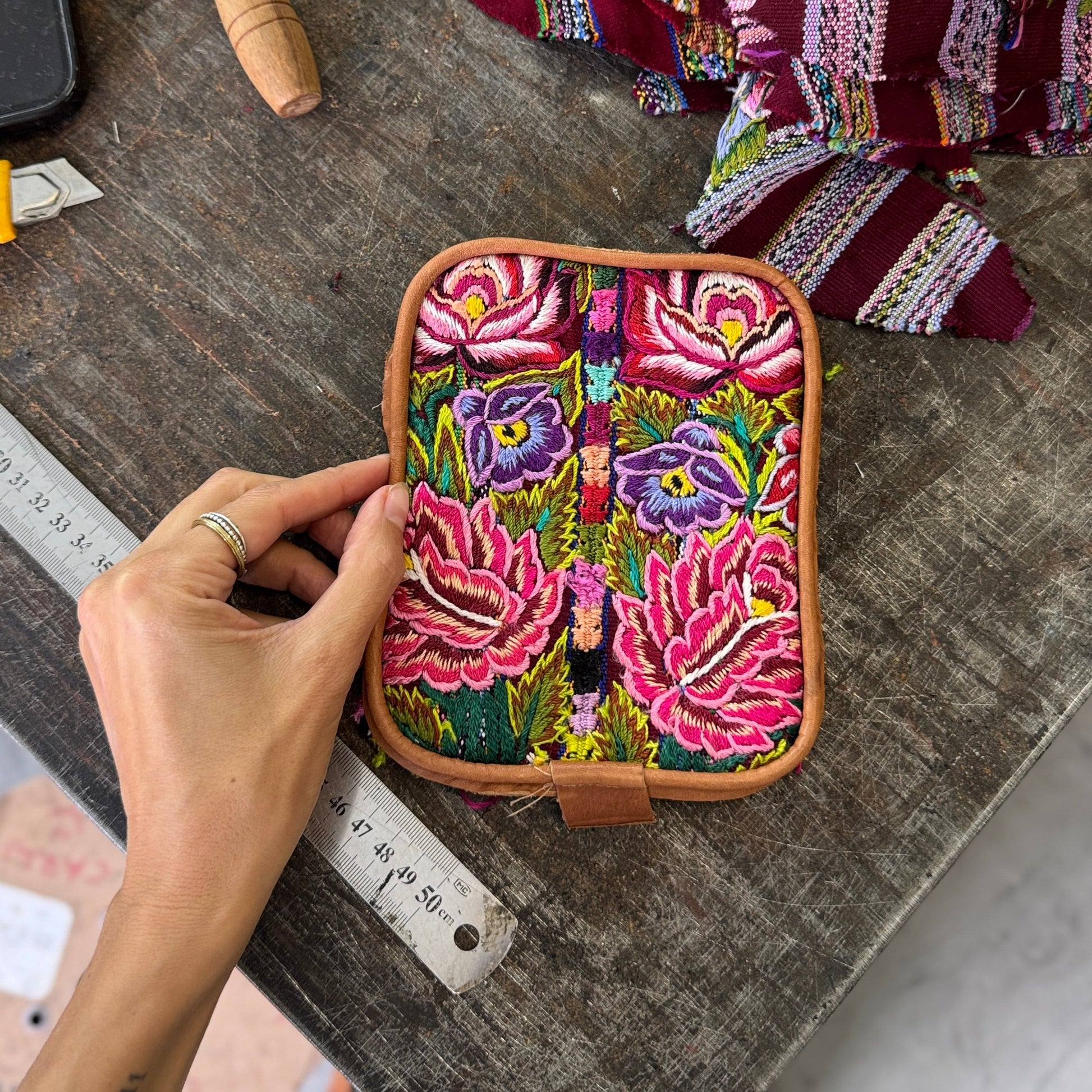 Colorful embroidered pouch held by a hand on a wooden surface with fabric and tools.