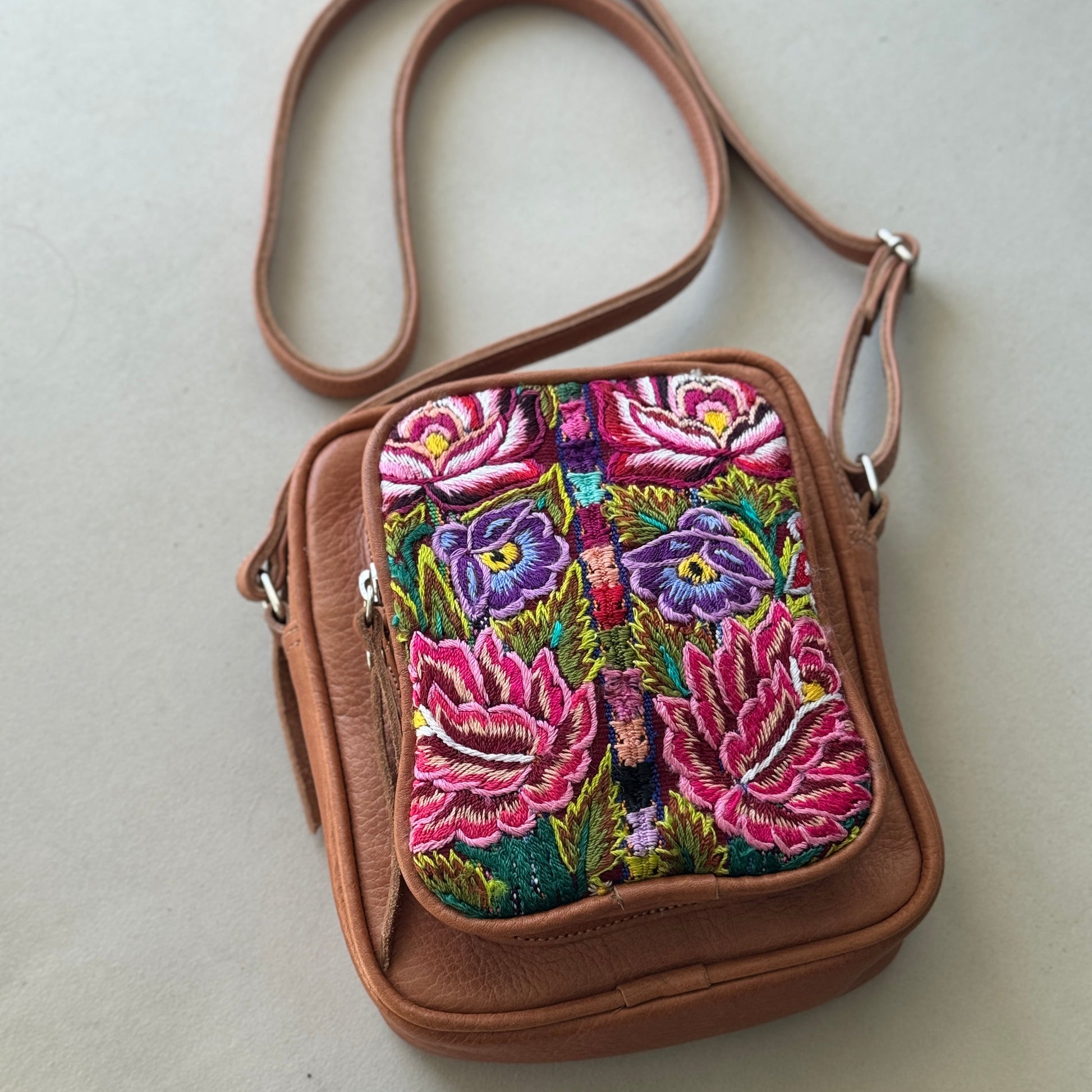 Brown crossbody bag with colorful floral embroidery on a light gray background
