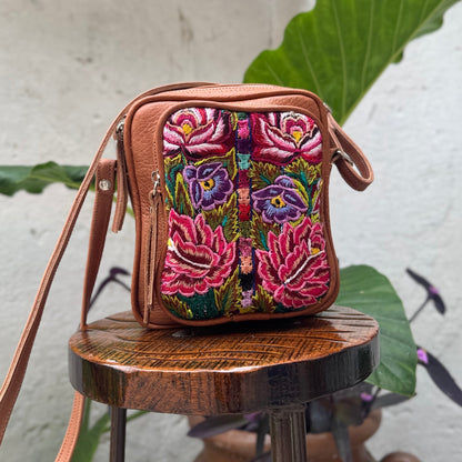 Embroidered handbag with floral design on a wooden stool against a white wall with plants.