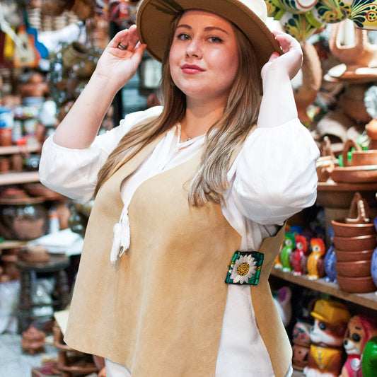 Woman wearing a tan vest with a sunflower design in a market setting with pottery and decor.