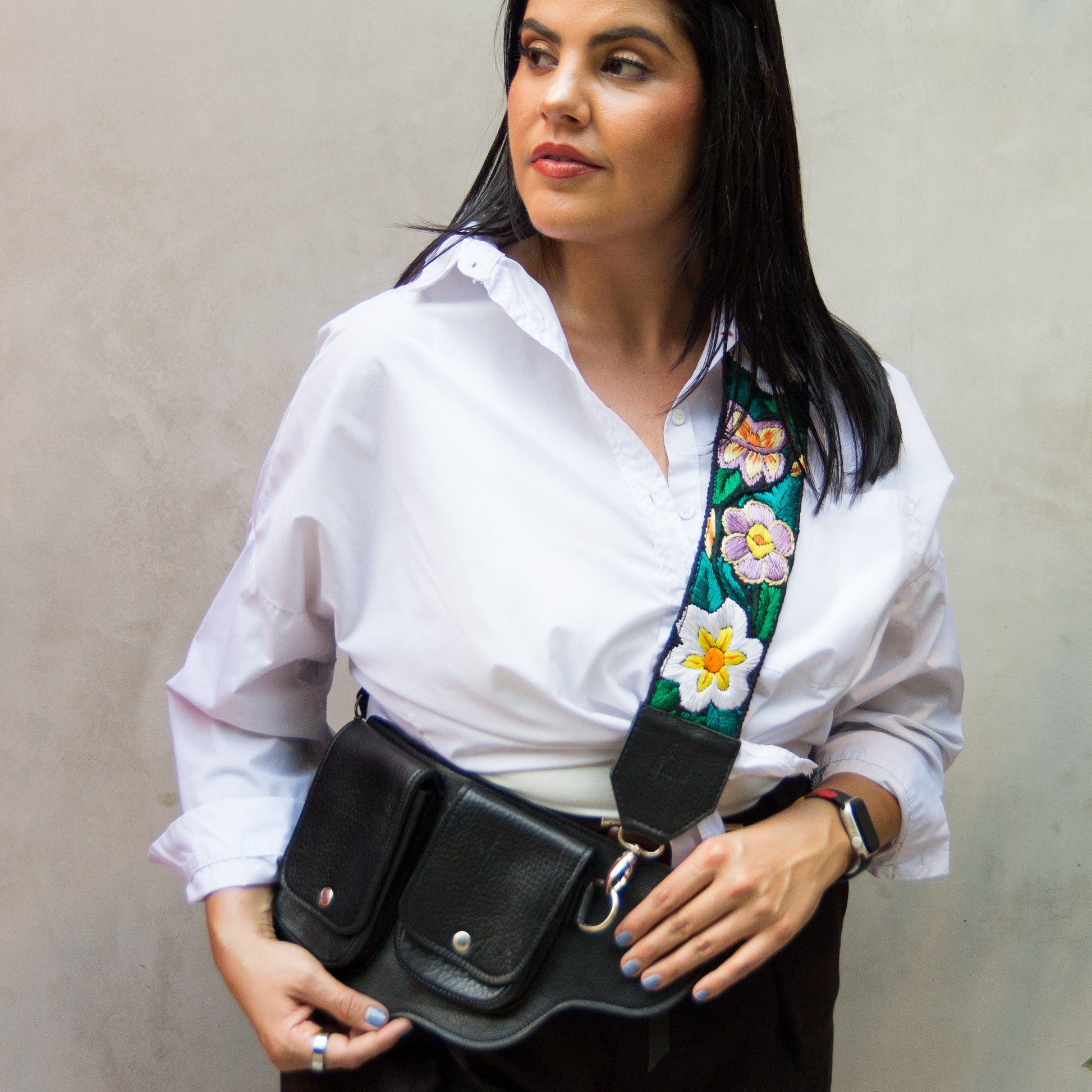 Woman wearing a white shirt with a floral tie and a black waist bag against a plain background