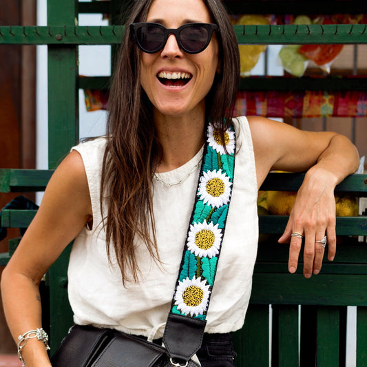 Woman sitting on a green bench wearing sunglasses and a black handbag with a floral strap.