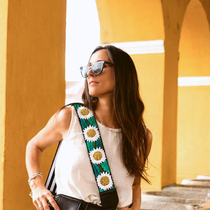 Woman with a black bag featuring a colorful strap with floral patterns, standing against a yellow wall.