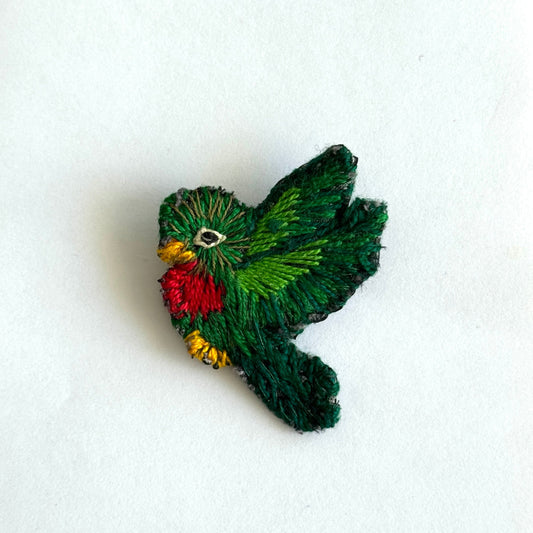 Embroidered green quetzal with red and yellow details on a white background