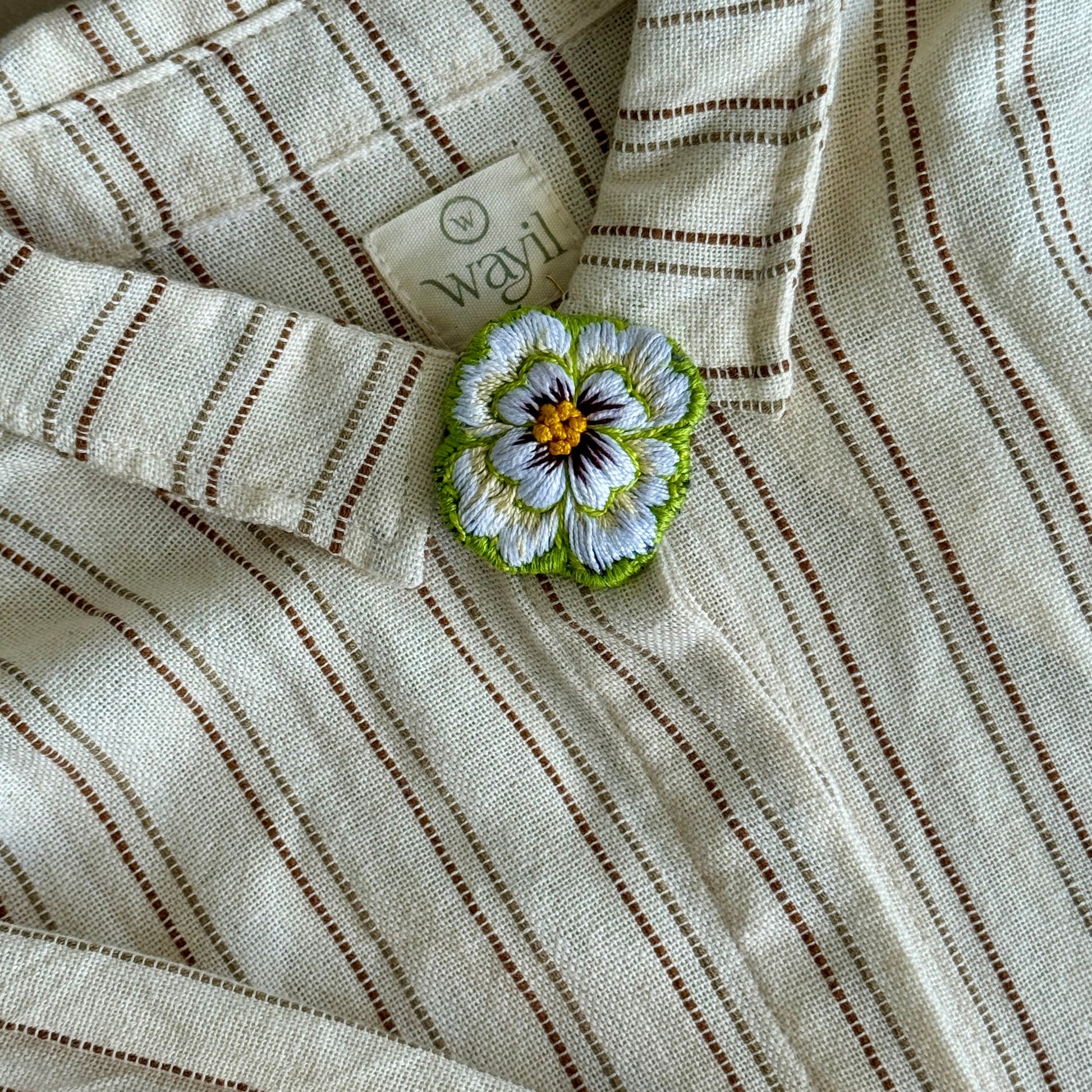 Close-up of a striped fabric with a floral brooch on a neutral background