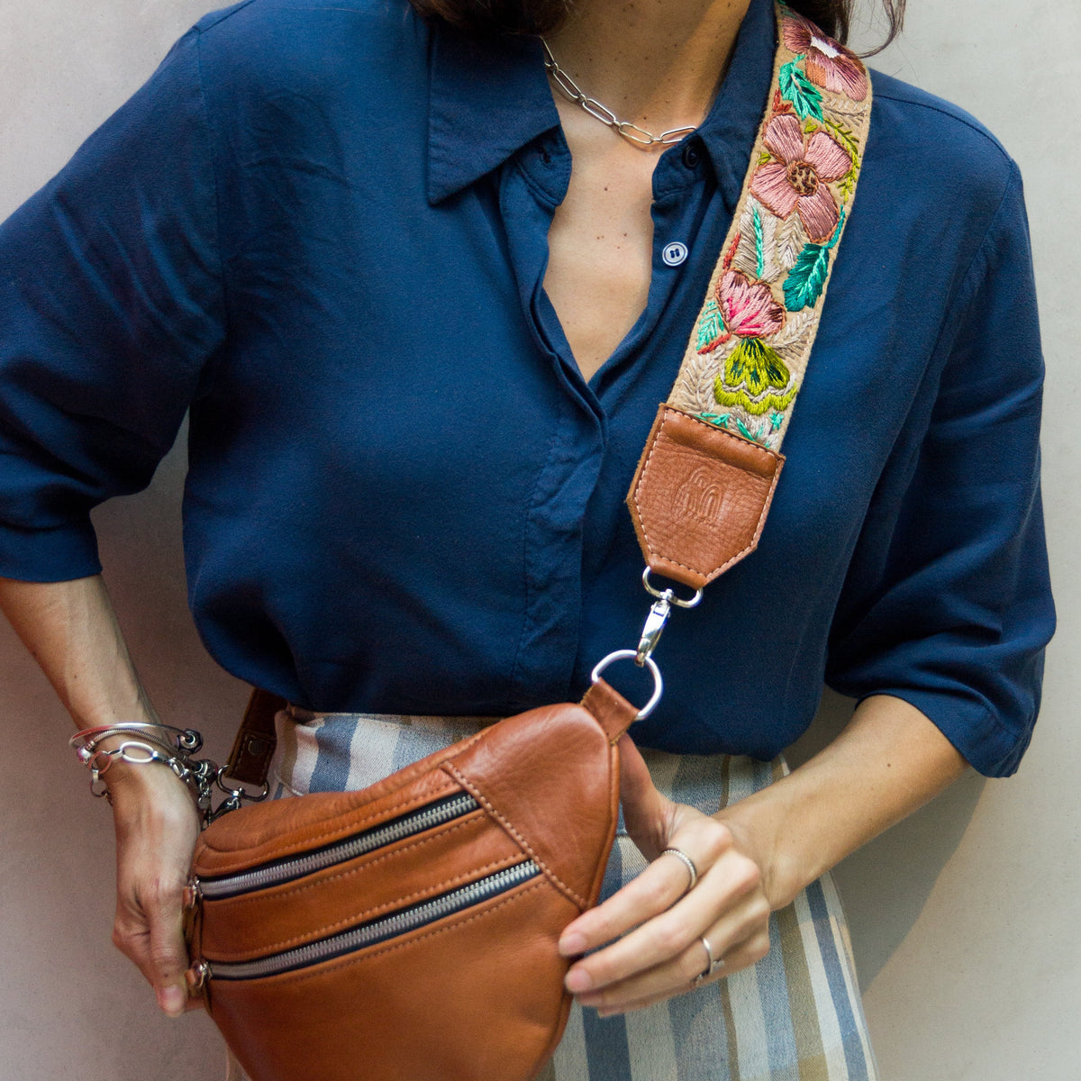 Woman wearing a brown leather waist bag with a colorful strap against a neutral background