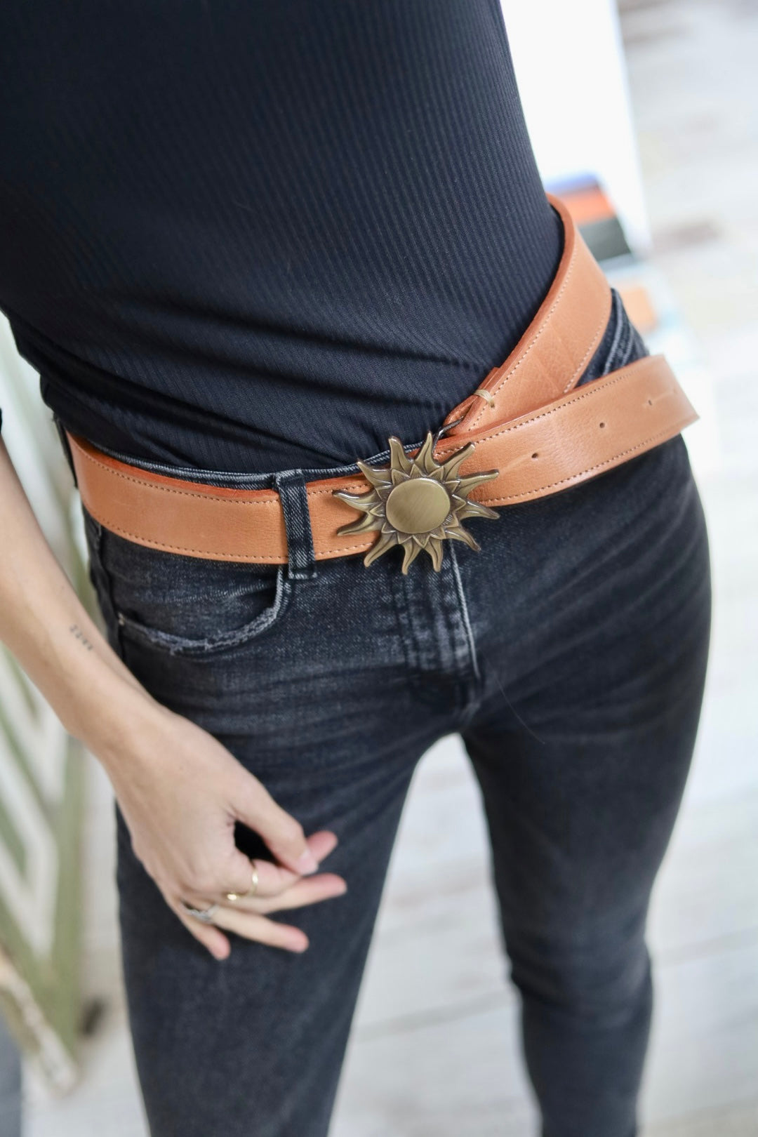 Person wearing a brown belt with a sun-shaped buckle on dark jeans.