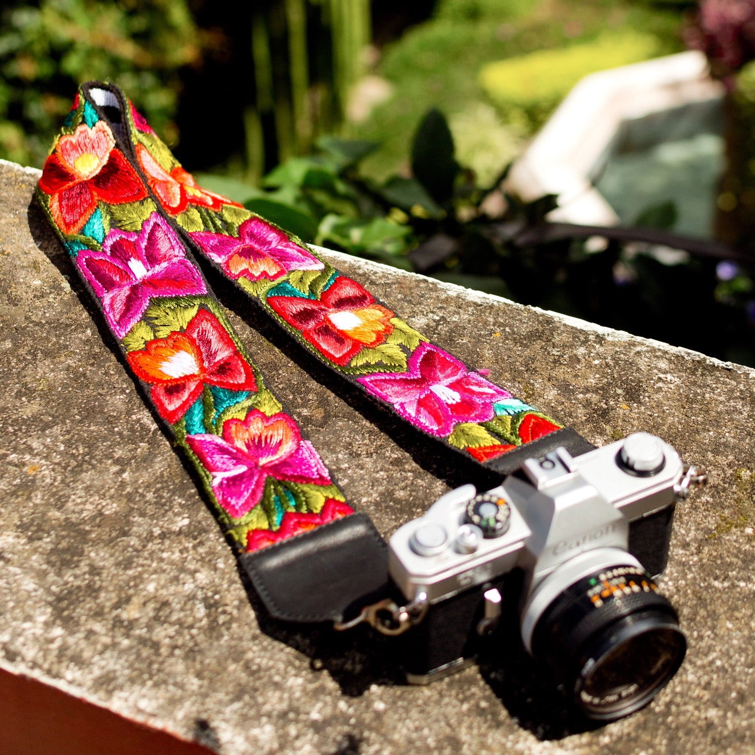 Camera with a colorful floral strap on a concrete surface with greenery in the background