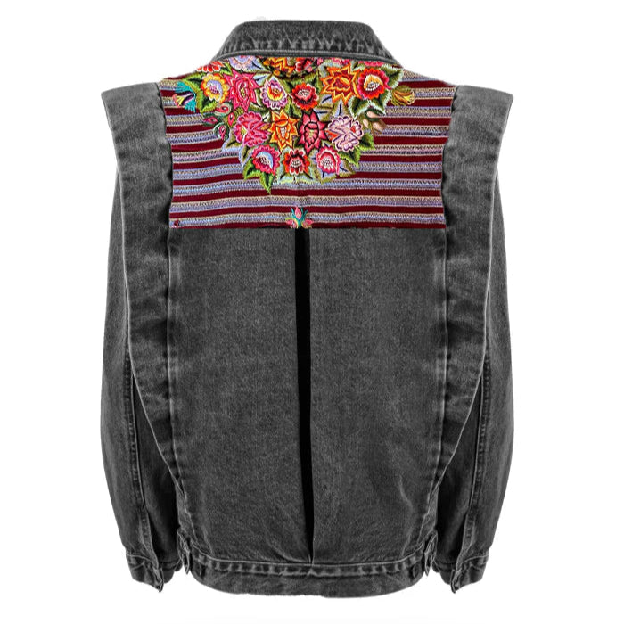 A gray denim jacket with a floral huipil design on the back, featuring a mix of solid colors and patterns.
