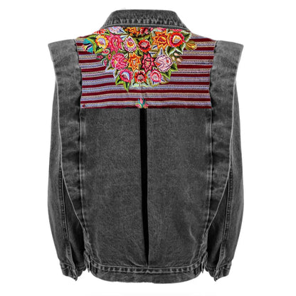 A gray denim jacket with a floral huipil design on the back, featuring a mix of solid colors and patterns.