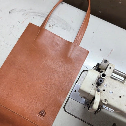 Brown leather tote bag on a sewing machine with a visible brand logo.
