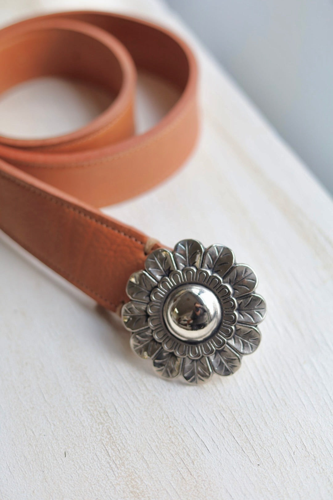 Brown leather belt with a decorative silver buckle on a white surface