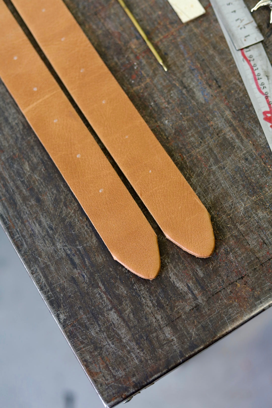 Two brown leather straps on a wooden surface with a ruler for scale.