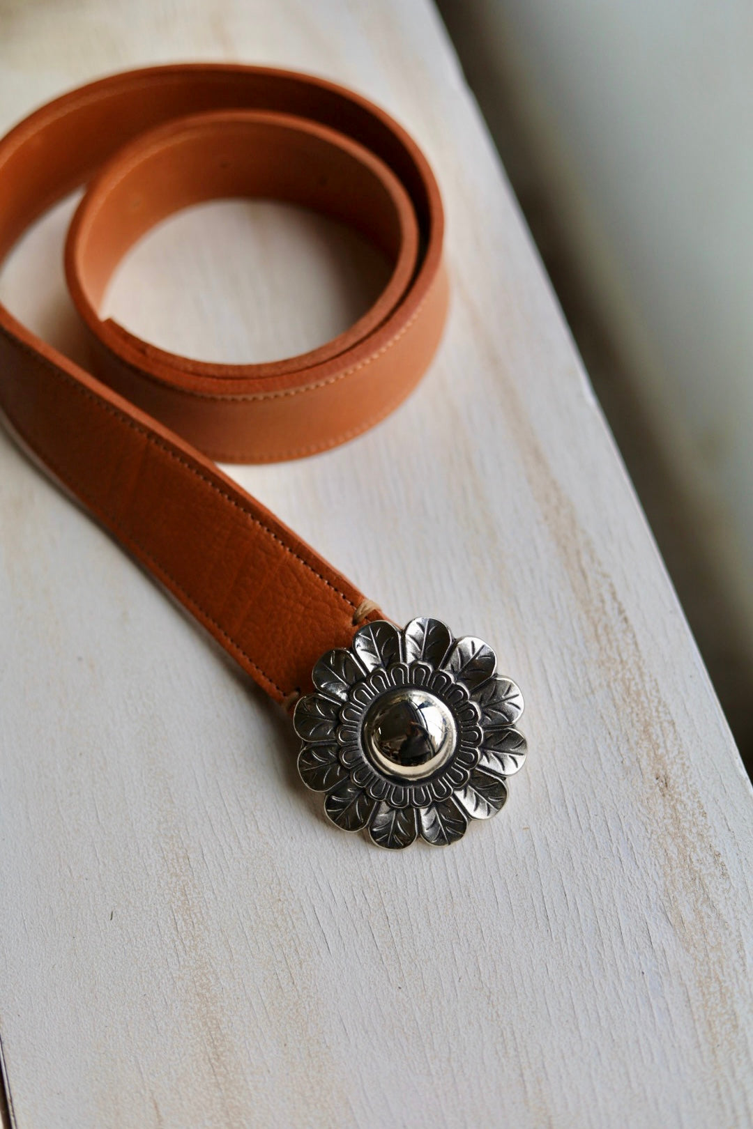 Brown leather belt with a silver floral buckle on a light wooden surface