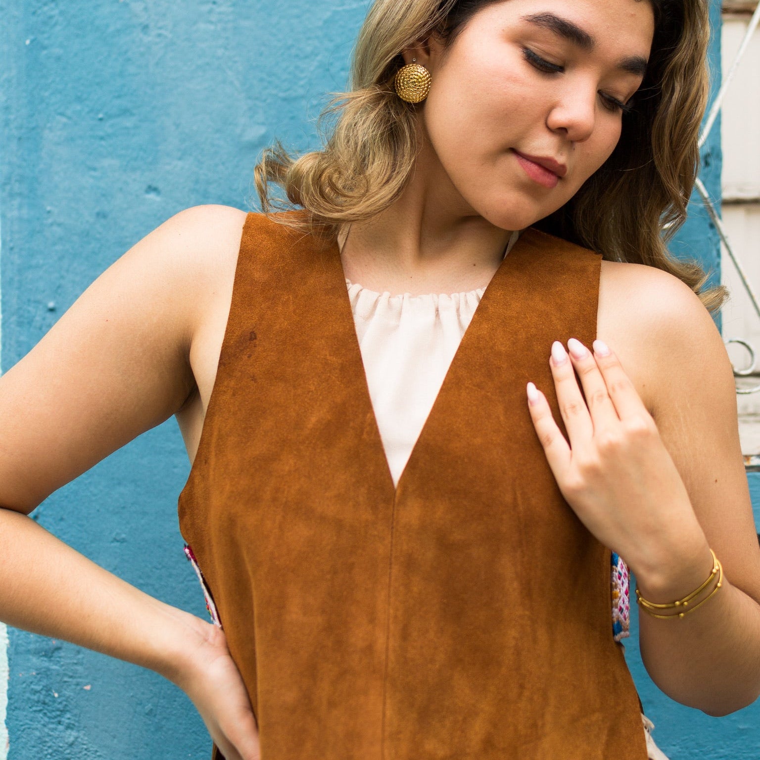 Woman wearing a brown sleeveless top against a blue wall