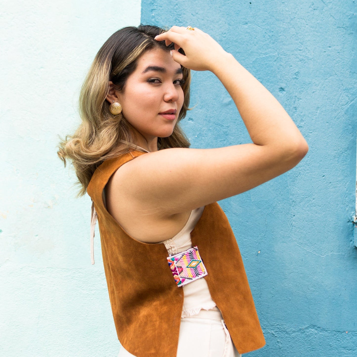 Woman wearing a brown vest against a blue wall
