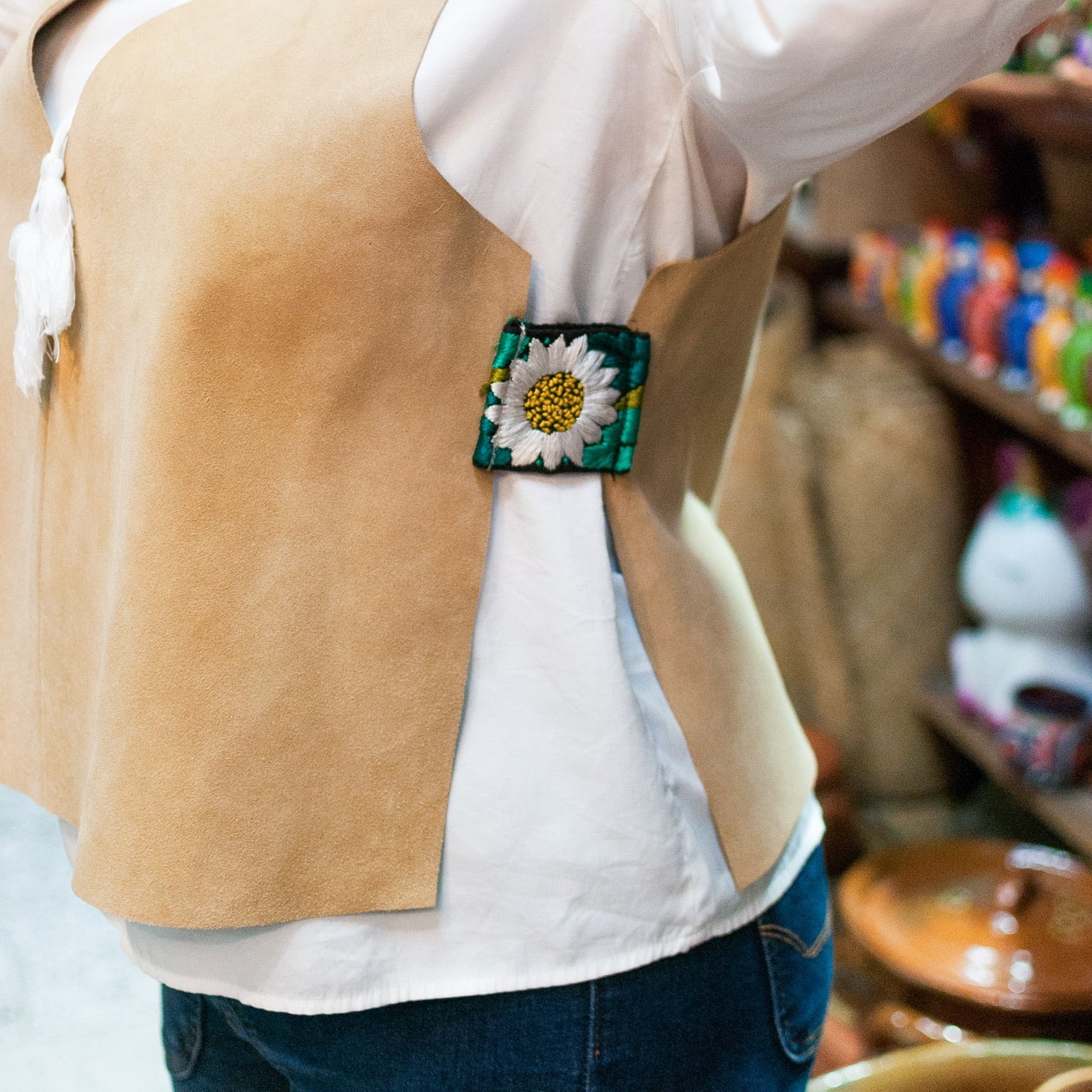 Person wearing a beige vest with a floral brooch, blurred background