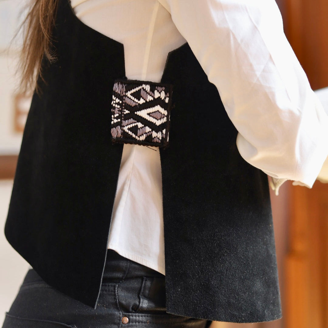 Person wearing a black vest over a white shirt with a patterned cuff.