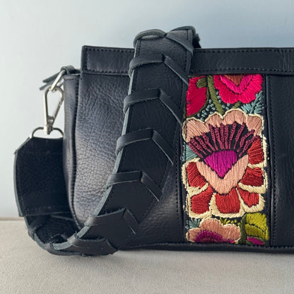 Black handbag with floral embroidery on a light gray background