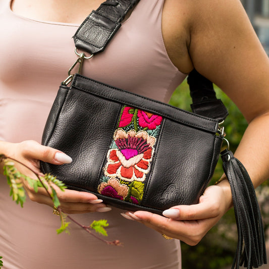 Woman holding a black handbag with floral embroidery and a tassel.