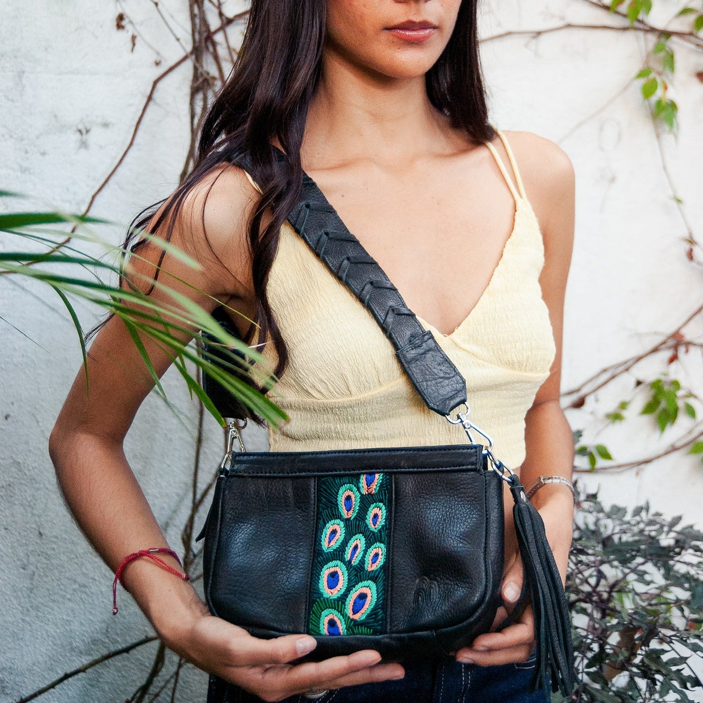 Woman holding a black handbag with peacock feather design against a natural background