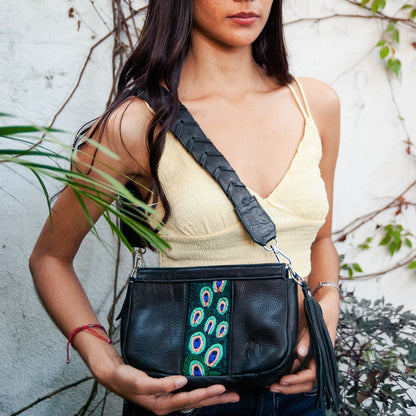 Woman holding a black handbag with peacock feather design against a natural background