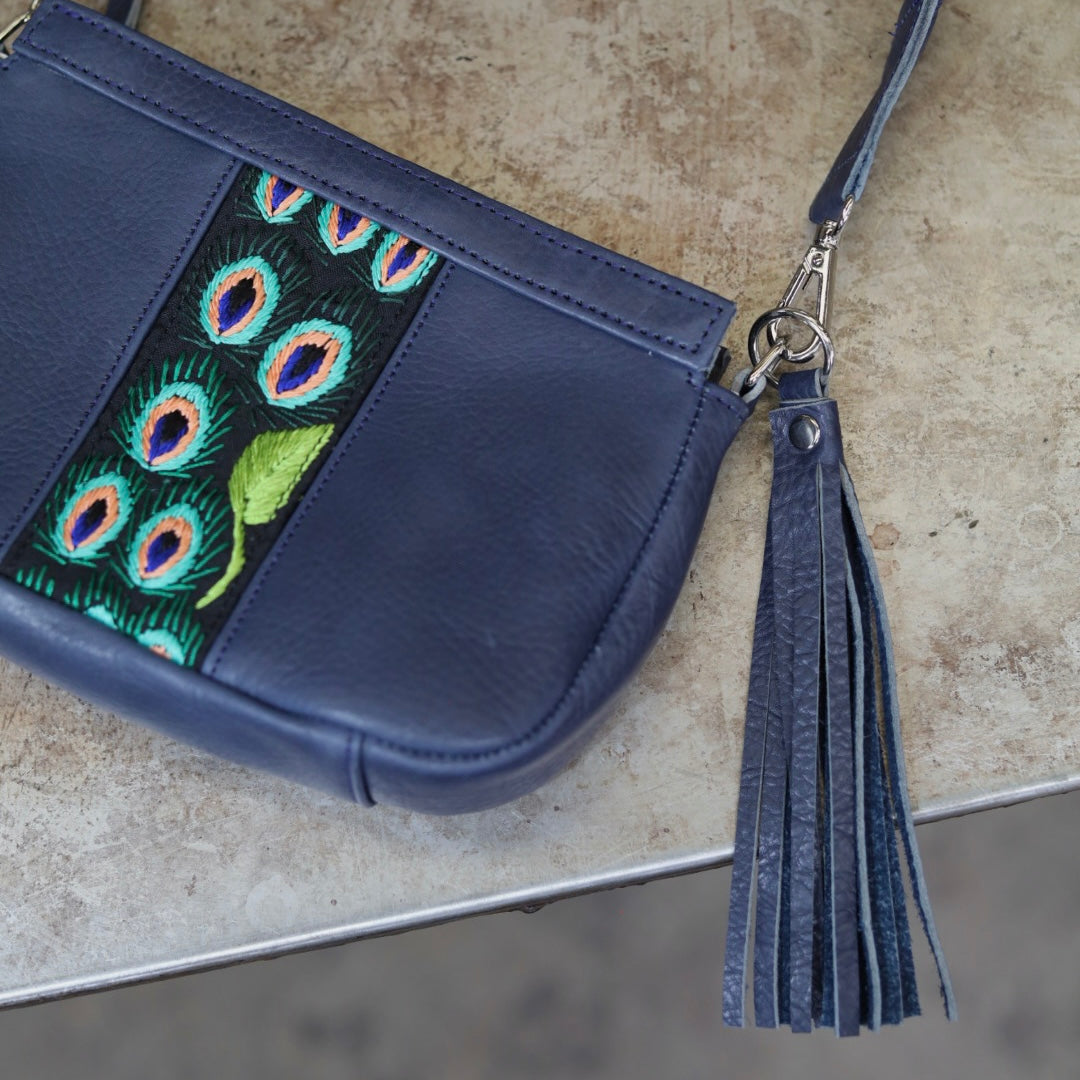 Blue handbag with peacock feather embroidery on a textured surface