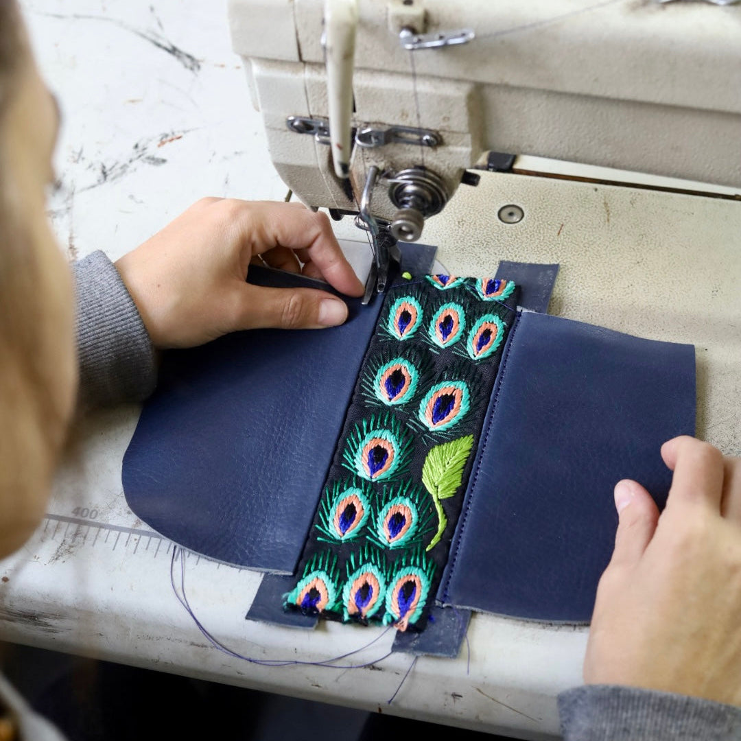 Person sewing a peacock feather design onto a blue fabric with a sewing machine.
