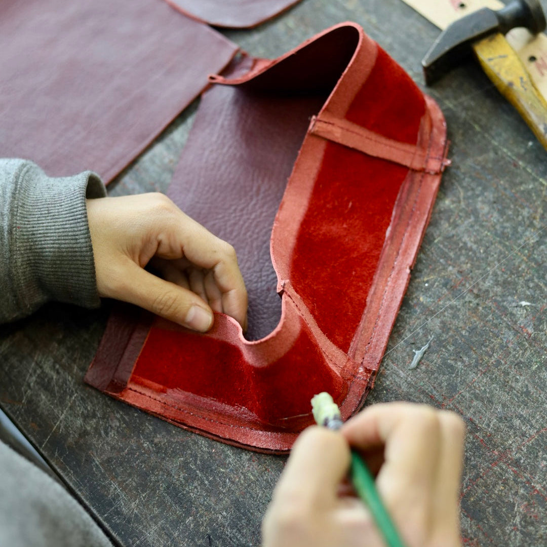 Person working on a red leather project with tools on a table