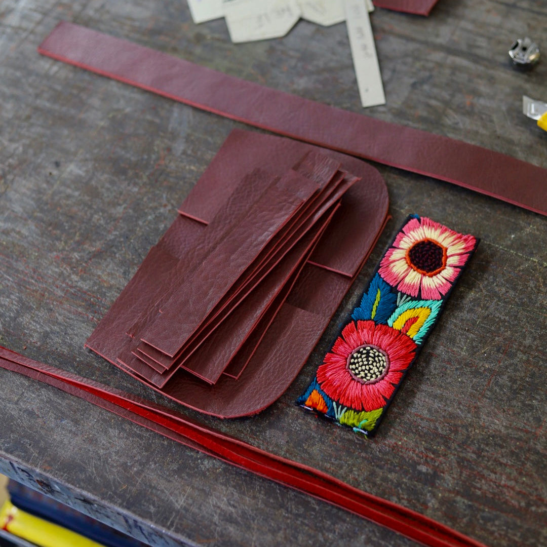 Colorful embroidered flower design on a leather surface with tools and materials.