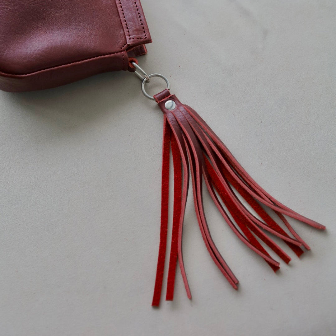 Red leather tassel keychain attached to a brown leather bag on a light gray background