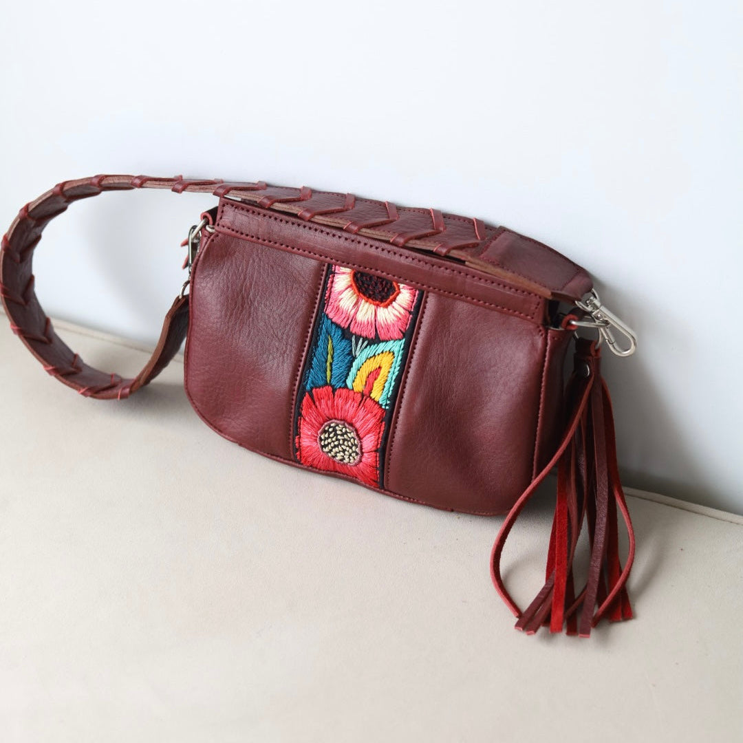 Brown leather handbag with colorful floral embroidery and red tassels on a light background