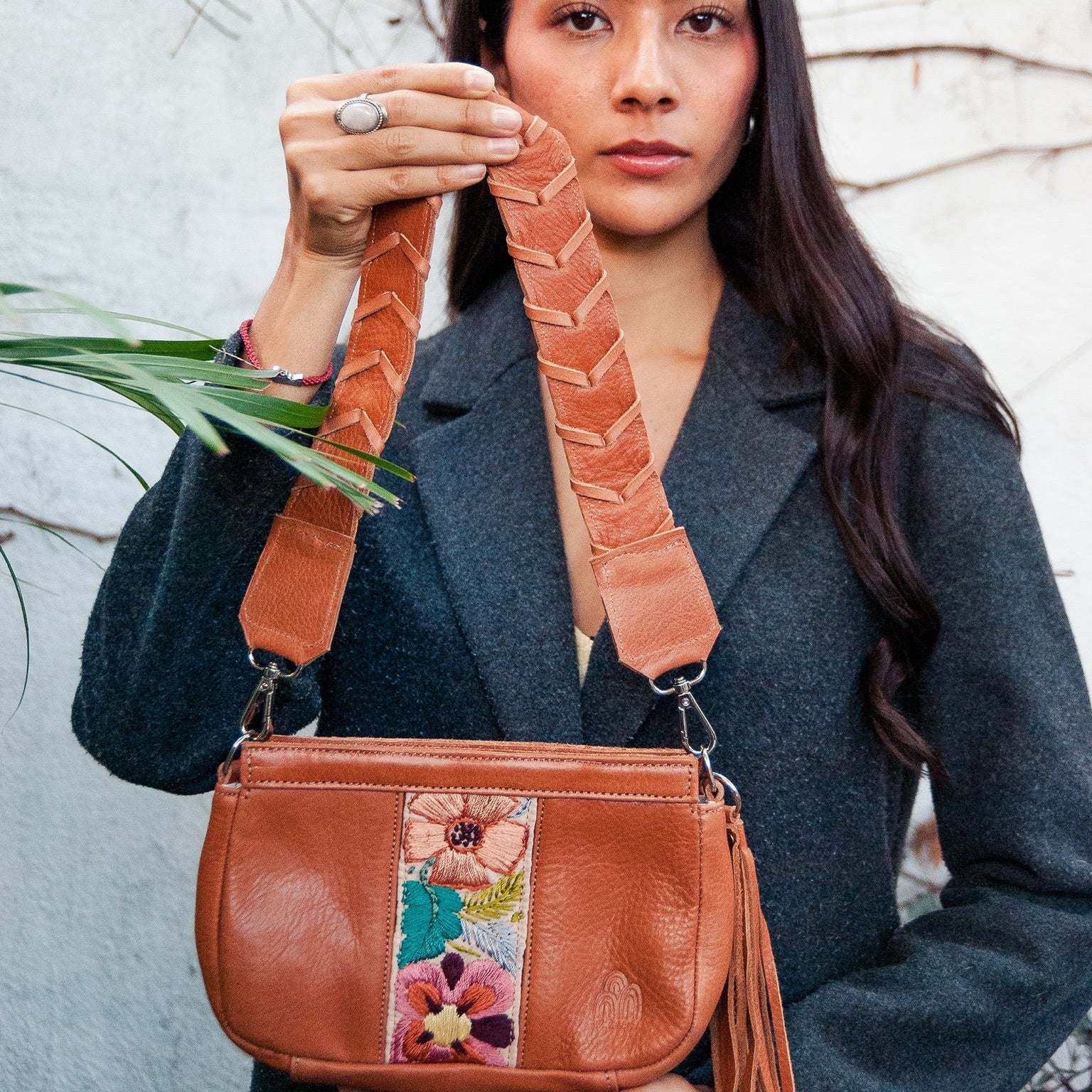 Woman holding a brown leather handbag with floral strap against a light background