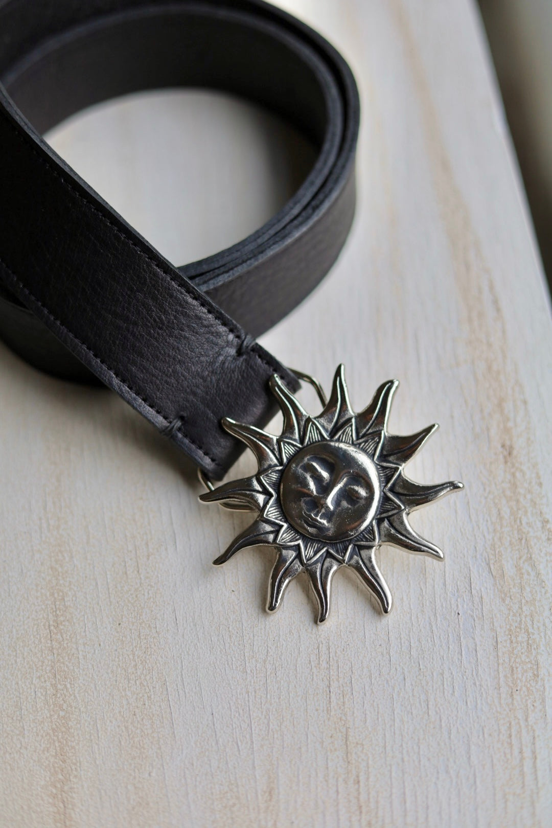 Black belt with a sun-shaped buckle on a light wooden surface