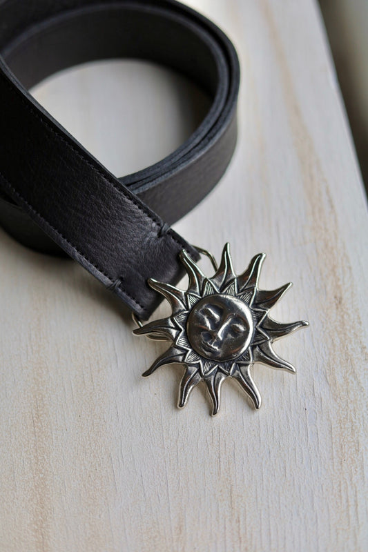 Black belt with a sun-shaped buckle on a light wooden surface