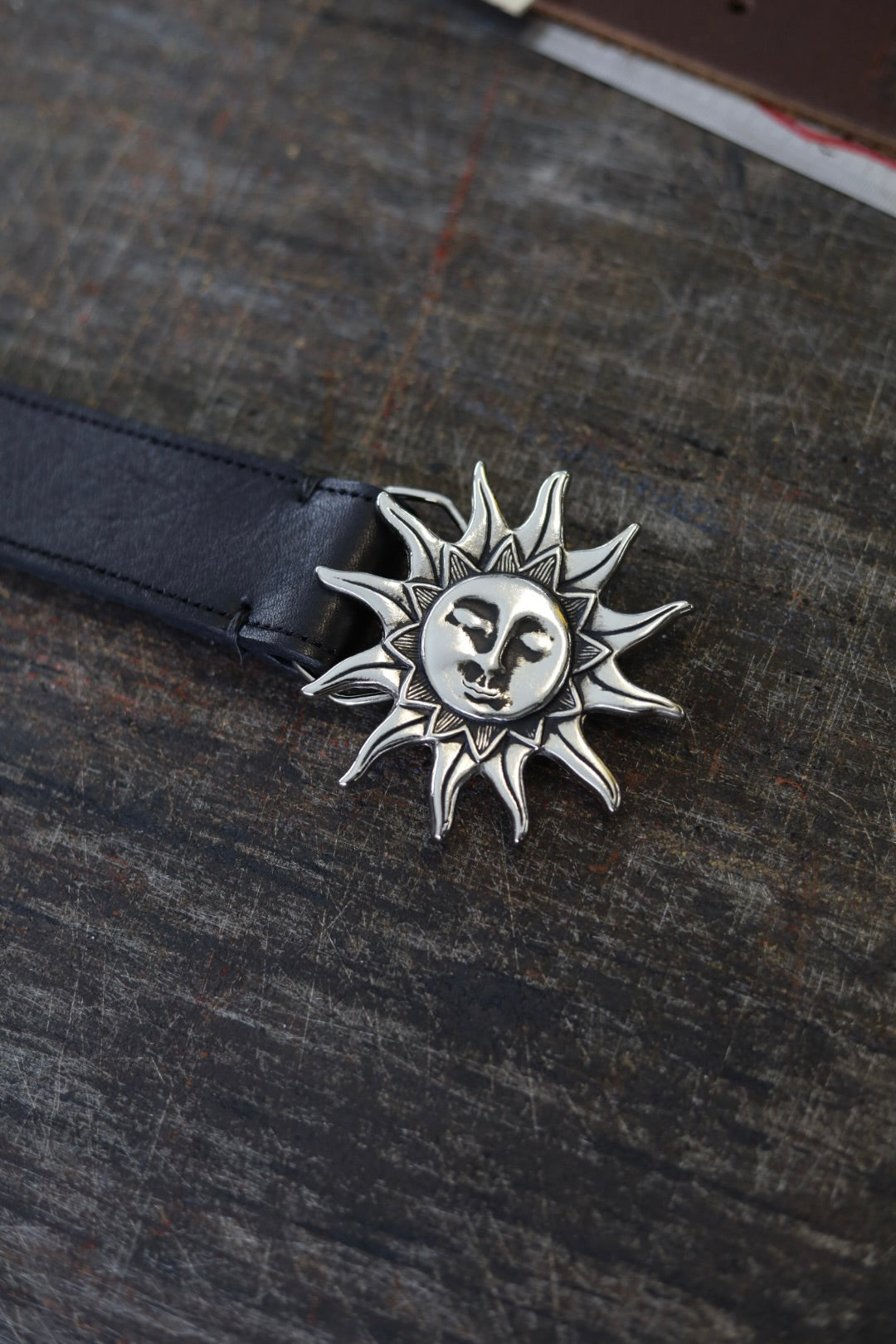 Silver sun-shaped pendant on a dark leather strap against a textured dark background