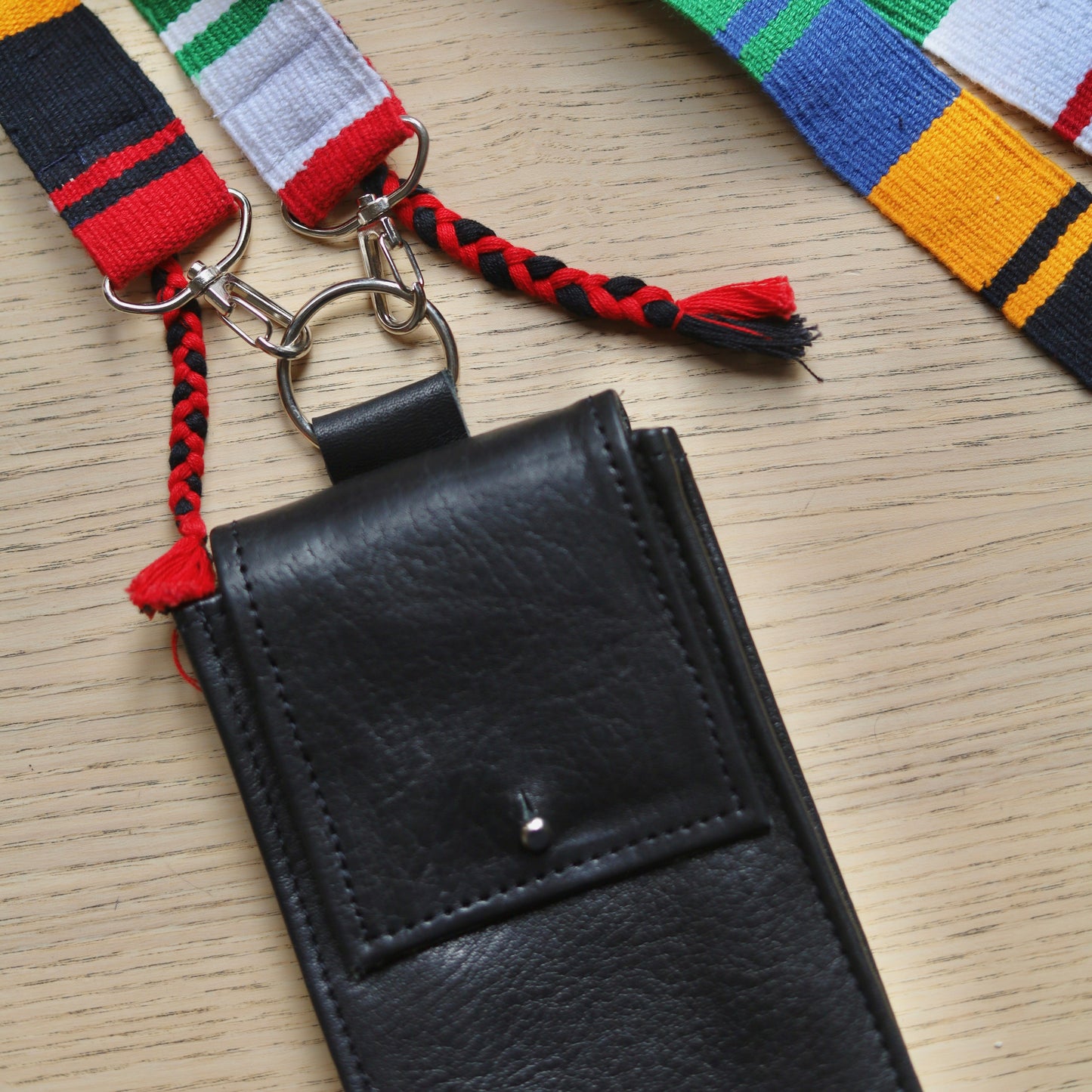 Black leather wallet with colorful braided strap on a wooden surface
