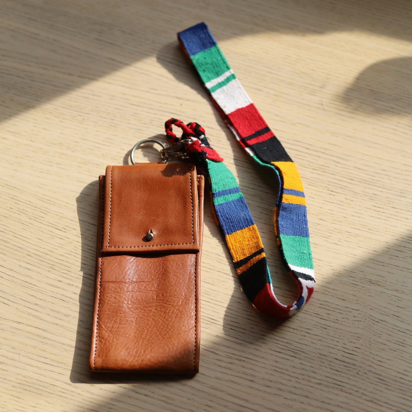 Brown leather pouch with colorful strap on a wooden surface