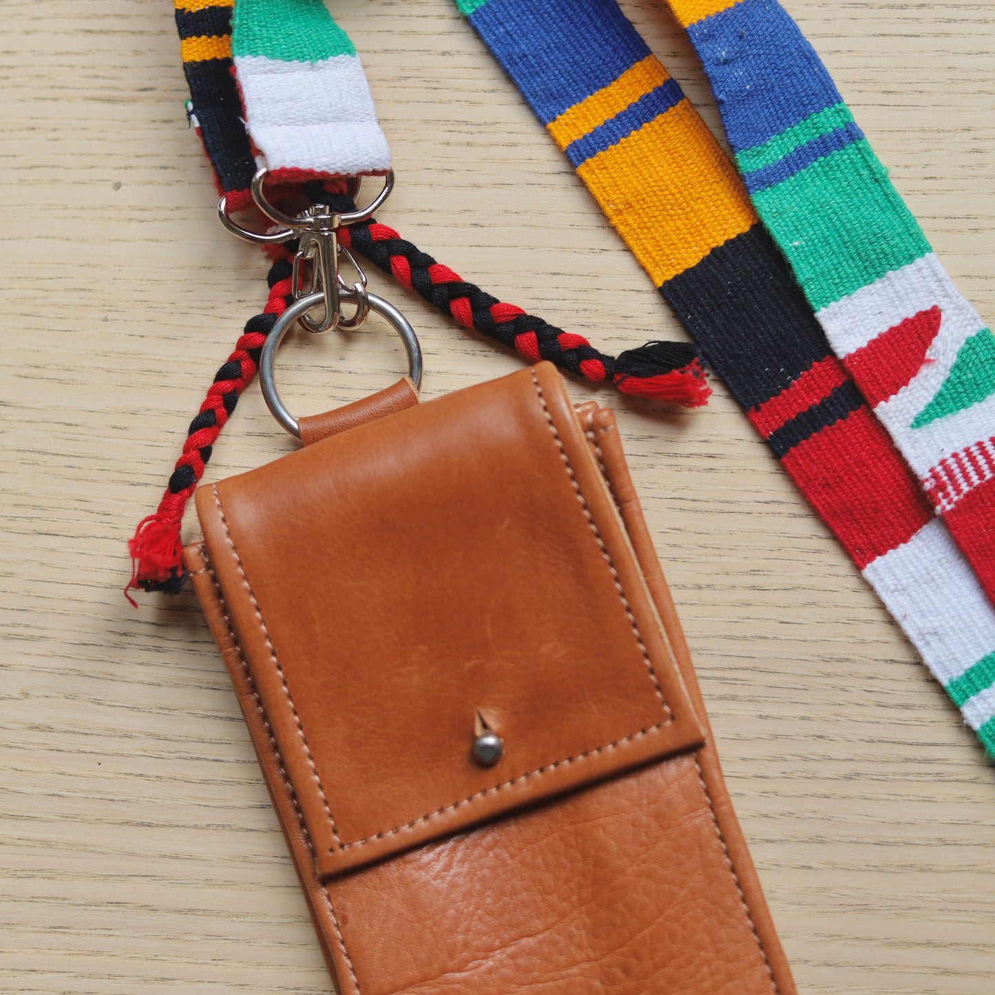 Brown leather pouch with colorful striped strap on a wooden surface