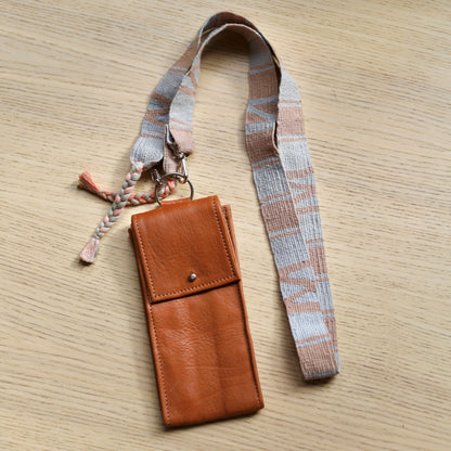 Brown leather phone case with plaid strap on a wooden surface