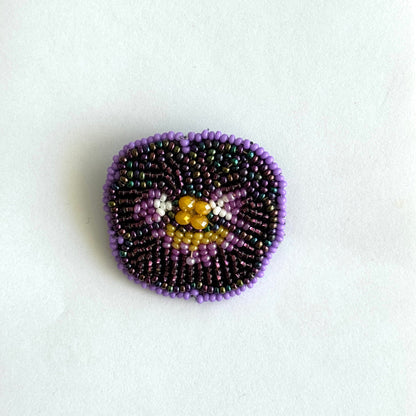 Beaded brooch with purple and gold design on a white background