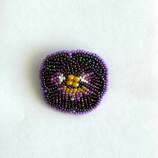 Beaded brooch with purple and gold design on a white background