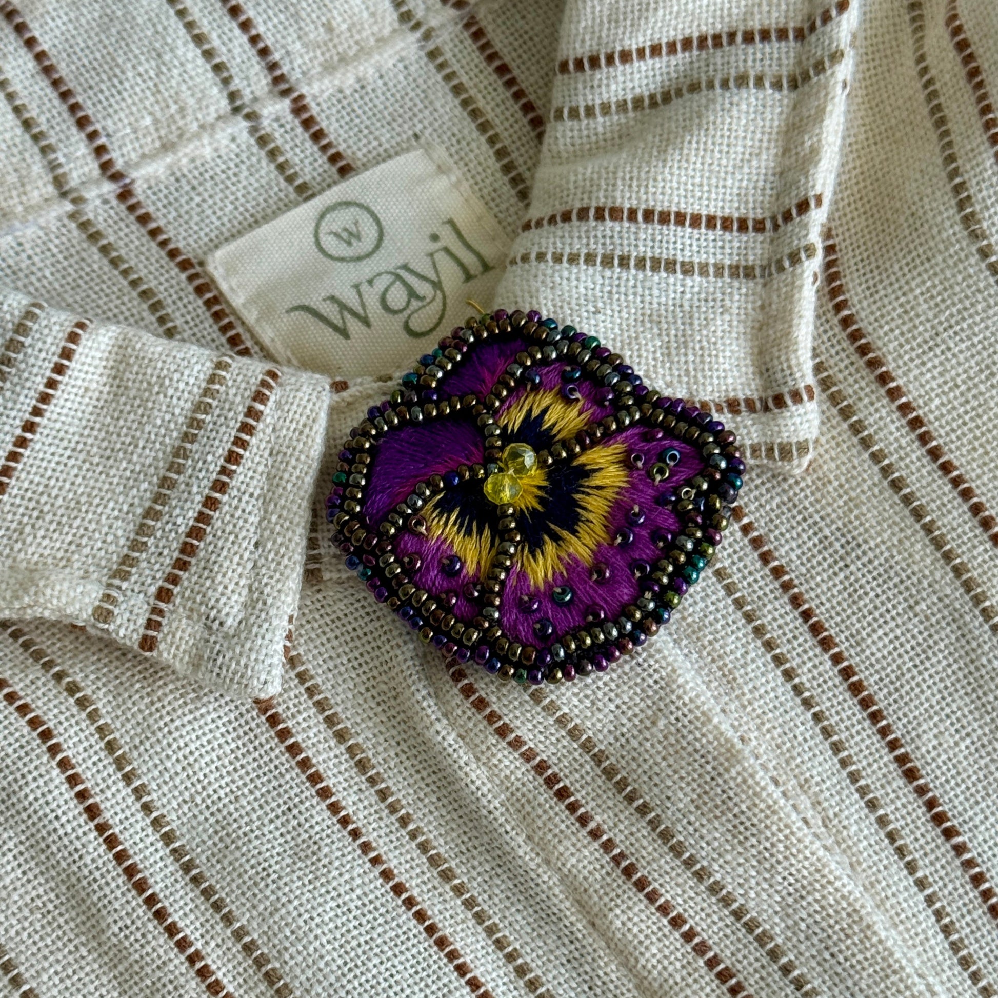Close-up of a white shirt with a beaded purple flower brooch and 'wayf' label.