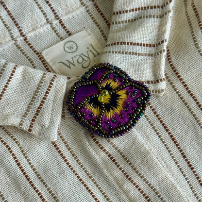 Close-up of a white shirt with a beaded purple flower brooch and 'wayf' label.