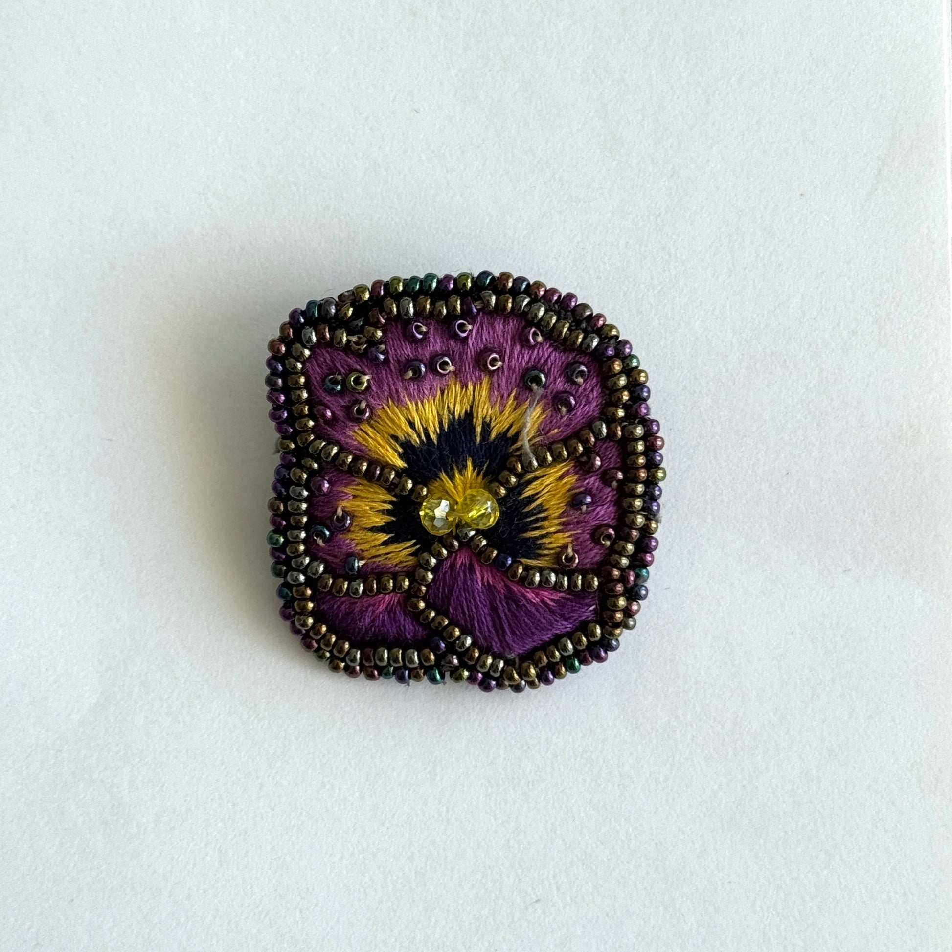 Decorative brooch with a purple and yellow flower design on a white background