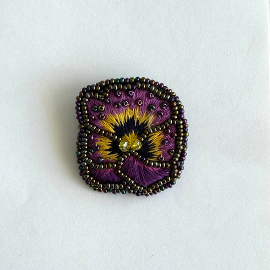 Decorative brooch with a purple and yellow flower design on a white background