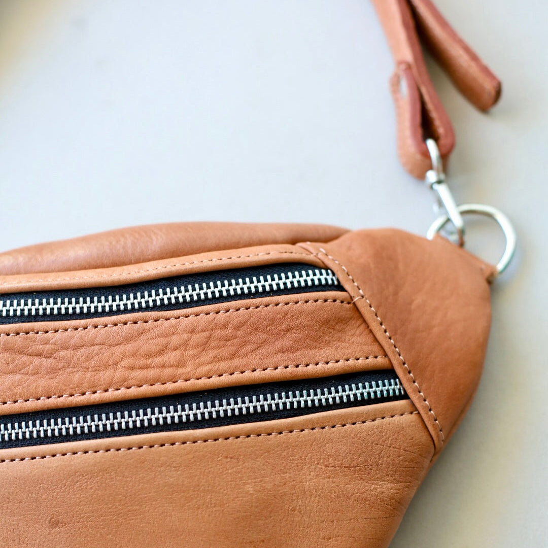 Brown leather fanny pack with a zipper on a light background